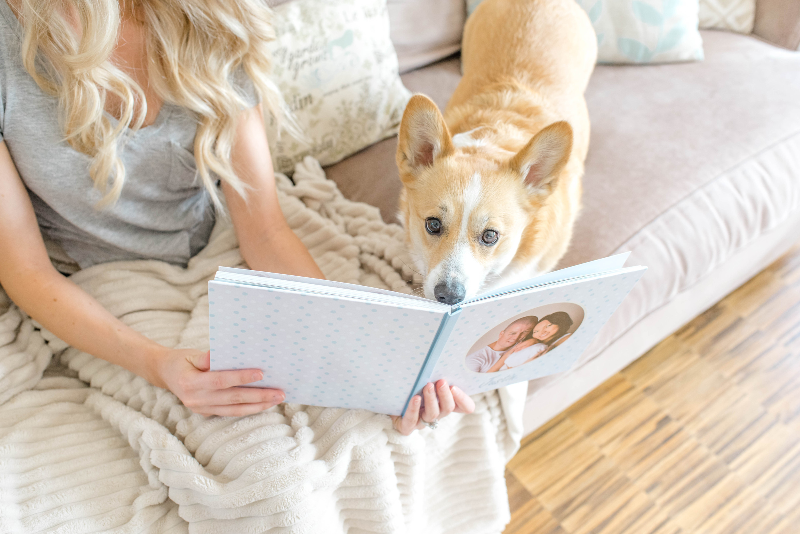Frau auf Sofa mit Hund schaut sich Fotobuch mit Bildeinband an