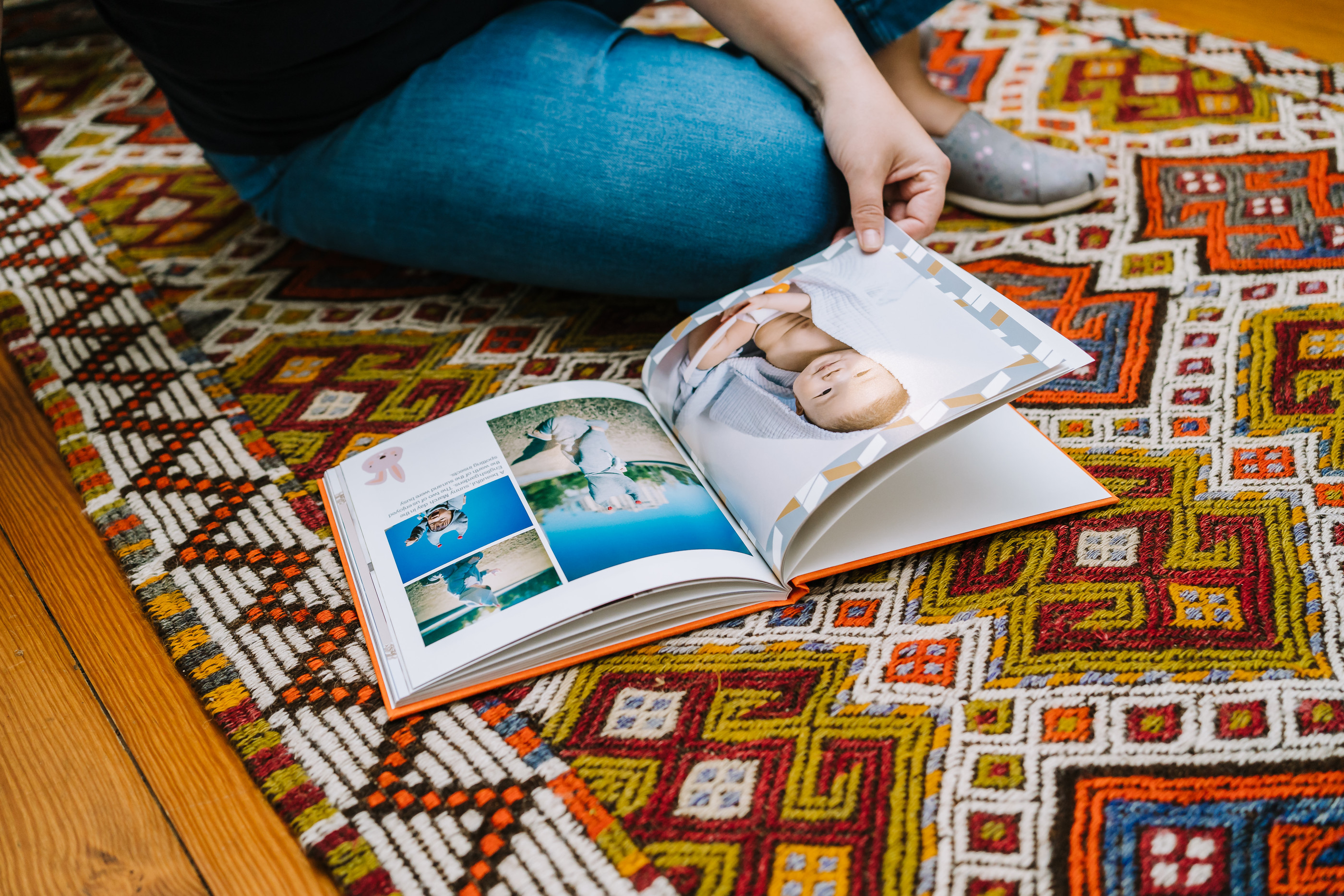 Frau schaut sich Baby Fotobuch auf Teppich an