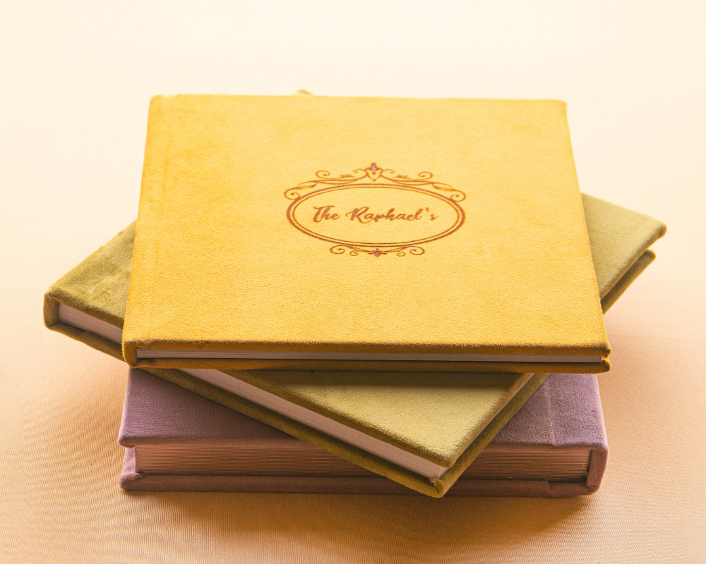 Stack of custom photo books in microsuede showing different sizes and colors, ideal for personalized album design