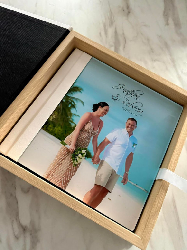 Modern acrylic wedding photo book with full-bleed beach image, ivory linen spine, and matching wood keepsake box.