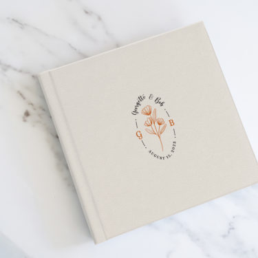 Layflat wedding album with cream vegan leather cover and custom UV-printed floral monogram design.