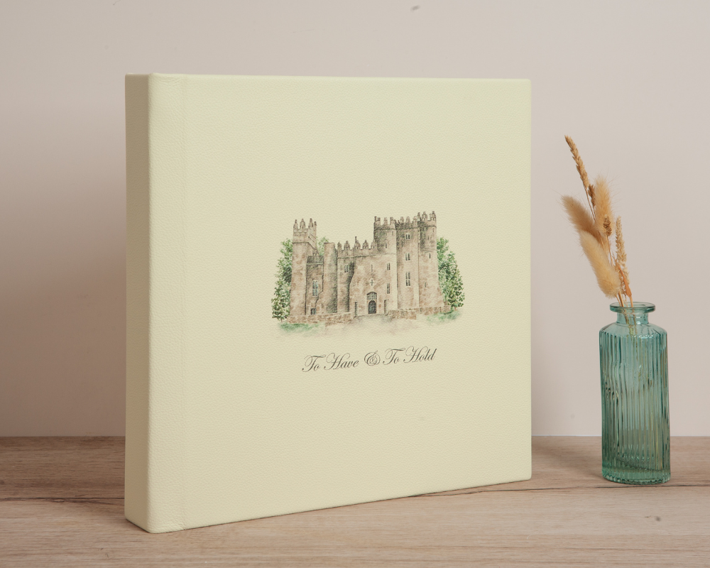 Wedding photo book with cream leather cover and a custom full-color sketch of a castle wedding venue, designed from a reference photo.