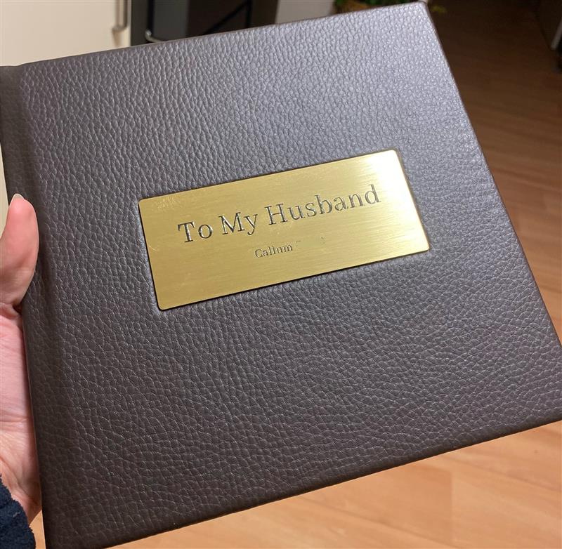 8x8 inch | 20x20 cm wedding photo book in dark brown vegan leather with brushed gold metal plate that reads “To My Husband – Callum.”