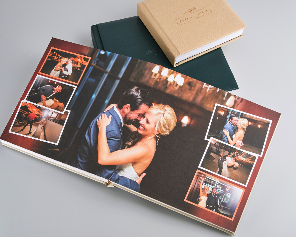 A custom wedding photo album with a collage-style layout featuring dancing and candid moments, displayed open on a table with two closed linen albums in the background.