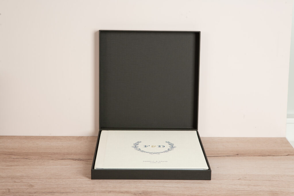 White vegan leather layflat wedding album in black clamshell box with multicolor UV printed laurel wreath design and monogram initials