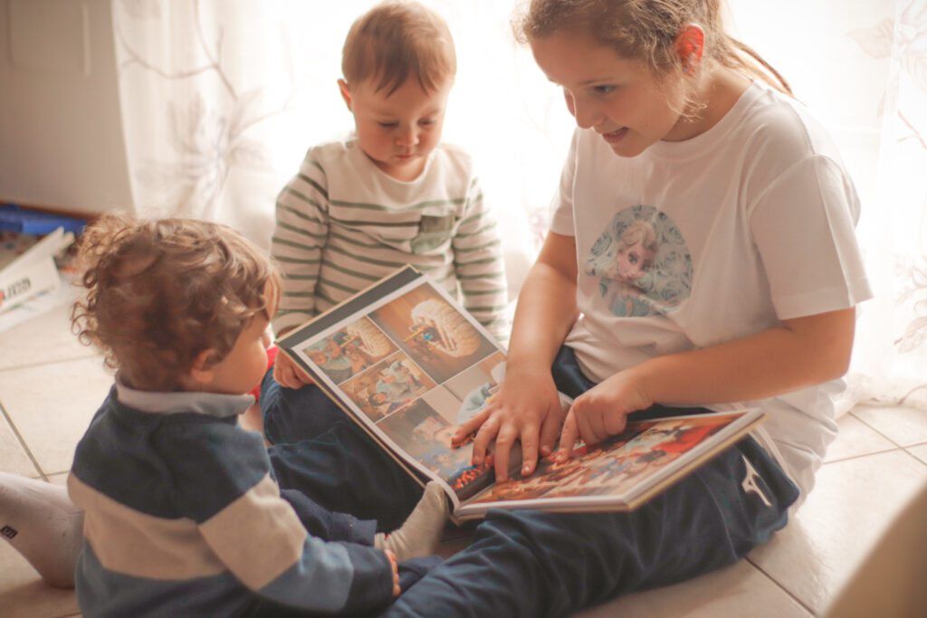 Three young children flipping through their family photo book, lsmiling as they look at photos from past years.