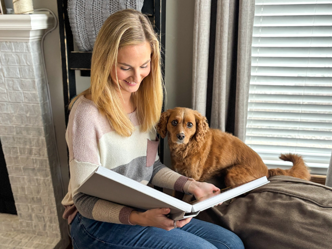 Woman browsing through her custom photo book while her dog rests beside her, showing how personal photo gifts become part of everyday moments.